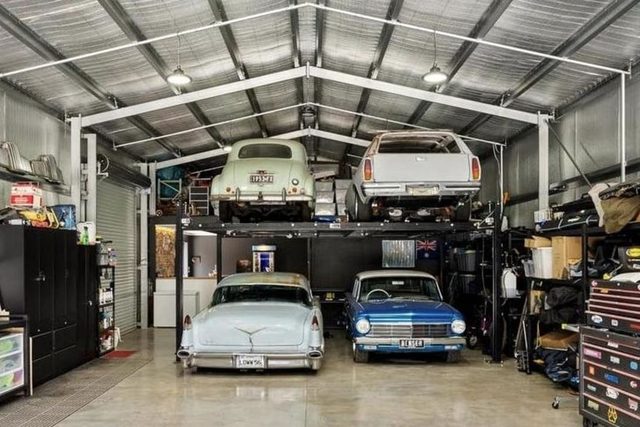 Four classic cars in a collector's garage, two of them up on a lift